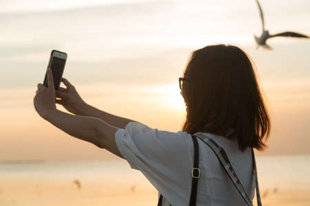 Woman were using phone camera. sun was falling behind as a bird flying in the sky.の写真素材