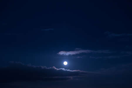 Full moon in the sky at night and a cloud hovering slightly.の写真素材