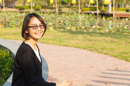 Portrait asian woman. happy and relax in park. smile and sit near sidewalk.