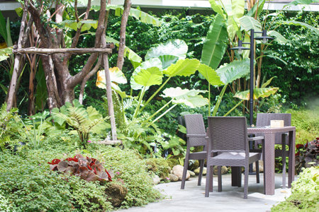 A serene garden scene featuring stylish outdoor dining set surrounded by lush greenery and tropical...