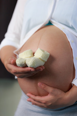 A pregnant woman gently holds pair of knitted baby booties against her round belly, symbolizing joy and anticipation of new life.の写真素材