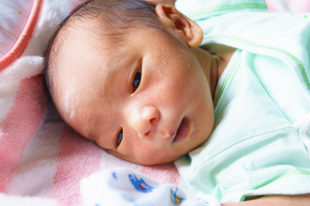 A close up of newborn baby with soft features, wearing light green outfit, lying on pink and white blanket. baby has curious expression, showcasing innocence and wonderの写真素材