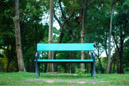 A vibrant green park bench surrounded by lush trees and grass, inviting relaxation in serene outdoor...