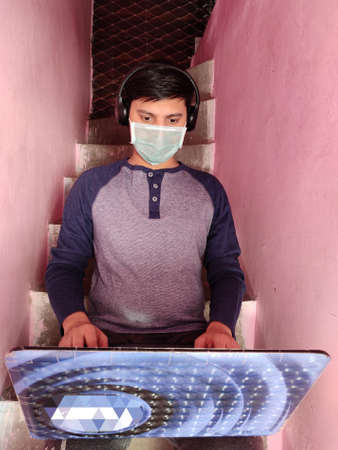 Man Working from home using laptop and Mobile, sitting on home stairs.Corona Pandemic , COVID 19 Spread,Blurred Background.の写真素材