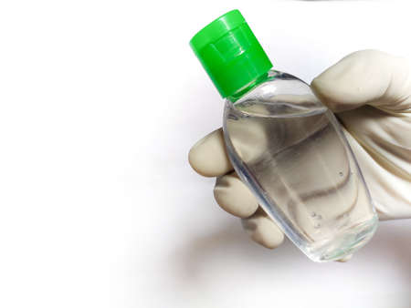 Hand in gloves holding tilted sanitizer bottle right screen, White background.の写真素材