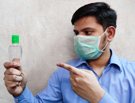 Man wear mask holding sanitizer in left pointing by hand right hand index finger, selective focus.の写真素材