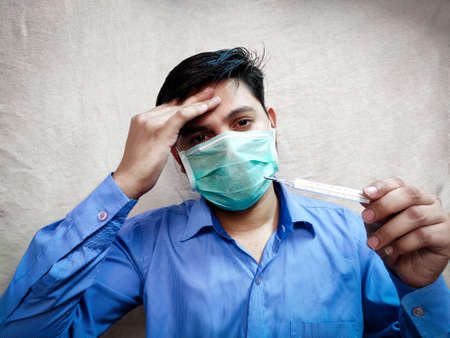 Man in fever Holds Analog Thermometer in hand checking fever reading high temperature by hand forehead,White background.の写真素材