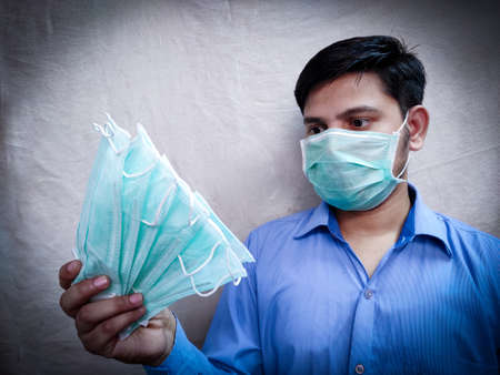 man in three layer surgical mask hold face mask packet or bunch in stretch hand. Selective focus , Blurred background.の写真素材