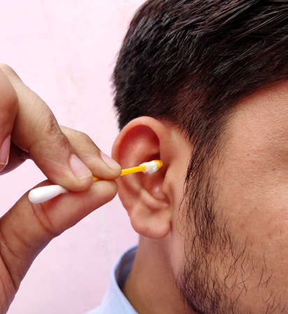 Man cleaning ear using ear swabs or cotton ear sticks on the light background. Ear care concept for Hygiene.の写真素材