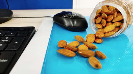 Almonds nut on office Table and in transparent box for healthy snacks diet plan on light colour...