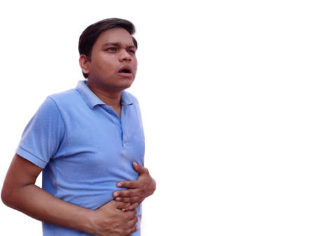 Image of young man wearing casual t-shirt touching his belly because of pain isolated over white background.の写真素材