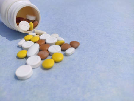 Bottle of pills on blue background for illness cure, Tablets spread on paper with space for text