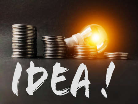 Saving money and finance management for future by light bulb glowing behind stack of coinsの写真素材