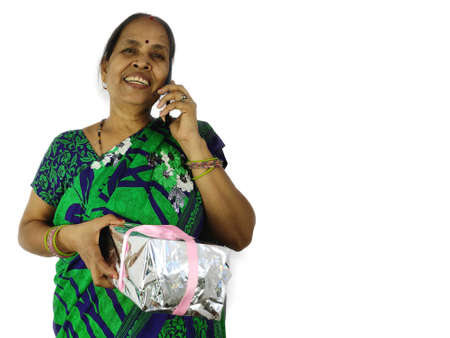 Indian Woman celebrate birthday or anniversary during video or phone call on mobile at home holding gift box present.の写真素材
