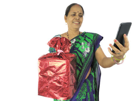 Indian Woman celebrate birthday or anniversary during video or phone call on mobile at home holding...