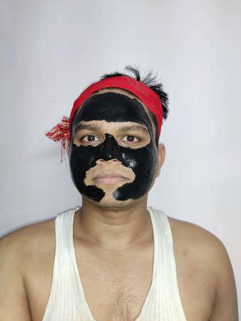 Young man with a black charcoal mask on his face on white background, Young and beautiful man with black peel-off mask on her face,の写真素材