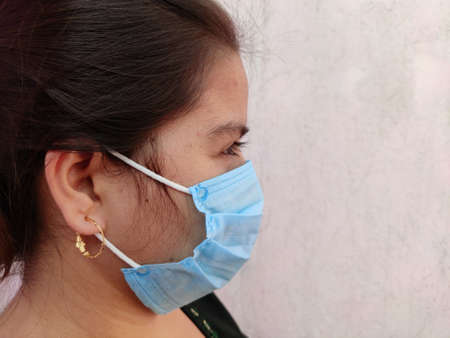 Side view of young indian woman face wearing medical face mask on white background. Protect your...