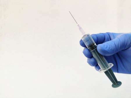 Syringe in hand wearing gloves on white backgroundの写真素材