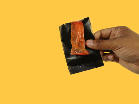 Condom disposal sachet used after sex for dispose off Condom, hand holding and keeping inside packet on yellow background with space for textの写真素材