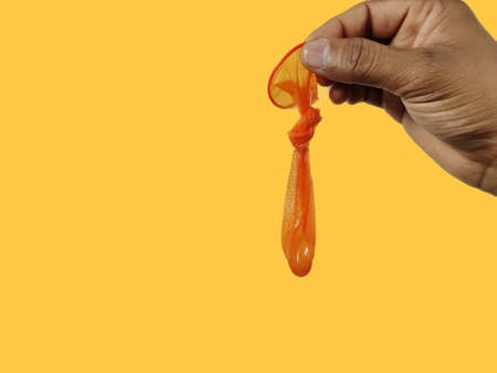 Man hand holding Orange Used condom against yellow background , space for textの写真素材