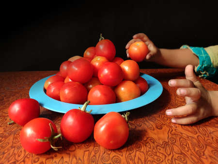 Vegetable Tomato arranged in plate by child hand on Textured wooden background with space for text.の写真素材