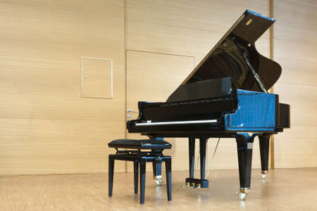 opened black grand piano with stool on a wooden concert stageの写真素材