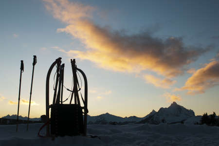 lonely bobsleigh standing in front of sunset landscape with mountains  and glowing cloudsの写真素材