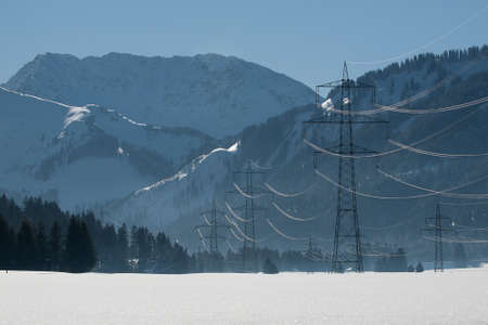 several power poles in a winter landscape with a lot of snow and mountainsの写真素材