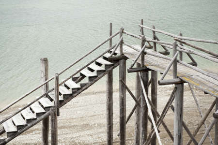 blocked obsolete wooden catwalk bridge at lake with less water and gravel at coastの写真素材