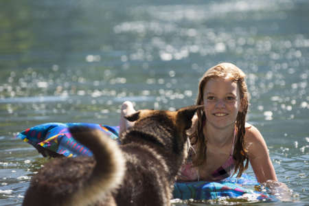 Pretty young teenage girl and her dog frolicking in the water of a lake in summer sunshineの写真素材