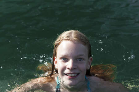 Attractive teenage girl with a lovely merry smile swimming in a lake with sunlight on the water and copyspaceの写真素材