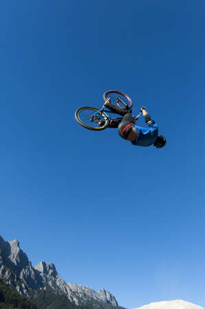 dirt biker makes a high backflip with blue sky and mountains in the background