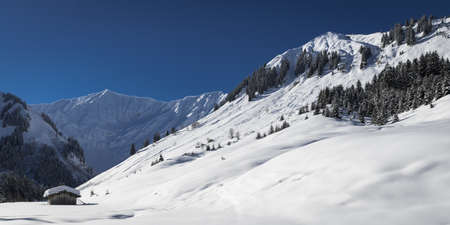 austrian snowy alp mountains at winter day with small hutの写真素材