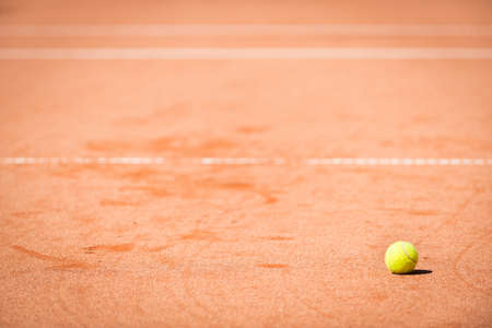 yellow tennis ball on orange sand and white linesの写真素材