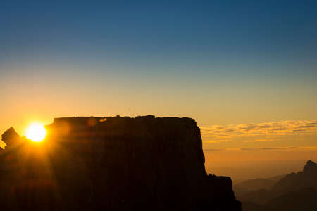sun shining between rocks on mountain at sunset