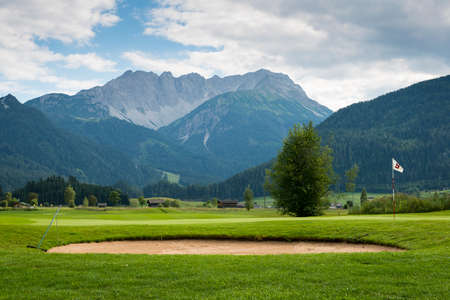 golf course with sand bunker and hole flag in mountain landscapeの写真素材