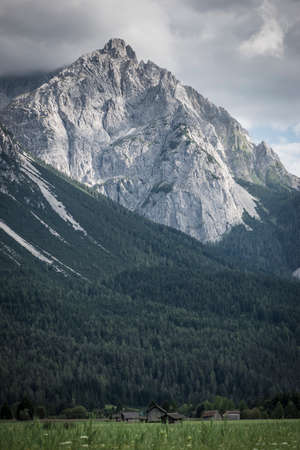 massive rock of mountain with clouds an meadow with chaletsの写真素材