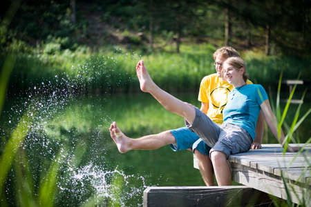 young couple splashing water at lake sitting on wooden peerの写真素材