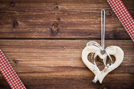 wooden heart hanging on sun burned planks with red white ribbonの写真素材