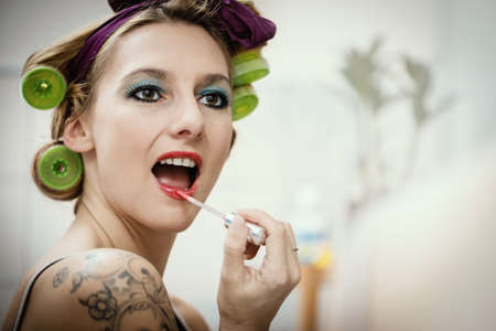 young attractive woman with hair roller is painting her lipsの写真素材