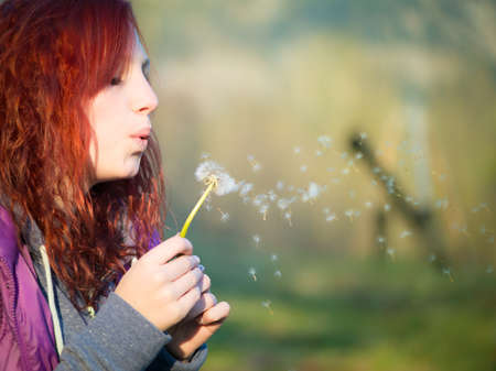 young teenager girl with red hairs blow to dandelion flowerの写真素材