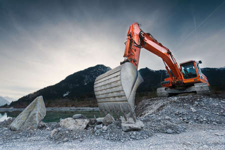 heavy organge excavator with shovel standing on hill with rocksの写真素材