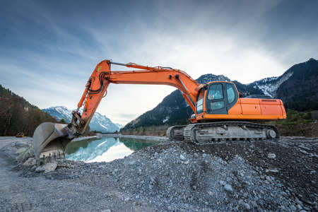 side view of orange shovel digger on gravel at lake and blue skyの写真素材