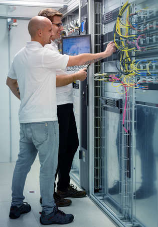 two IT professionals with notebook in server data center room solving a problemの写真素材