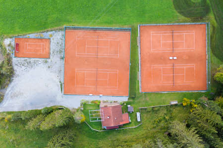 bird's eye view to four orange clay tennis courts in green meadow landscapeの写真素材