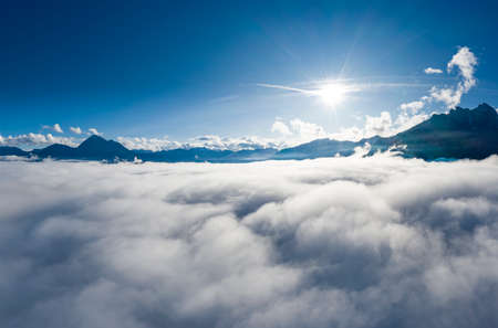 aerial view over cloud bank to tirol mountain alps with sun beamsの写真素材
