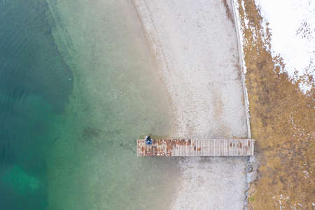 thoughtful person sitting on dock at shore of silent lake in winterの写真素材