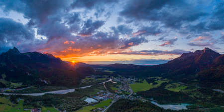 hiding sun behind mountain chain hahnenkamm with view to village pflach in reutte tirolの写真素材