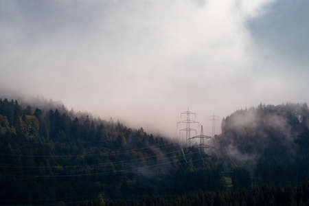 Electricity pylons in misty and cloudy wooded hills in autumnの写真素材
