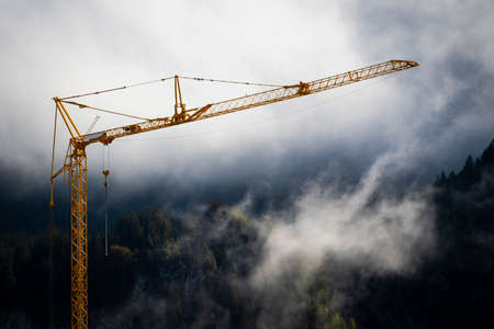 orange construction site crane with foggy misty forest in background with fading white to topの写真素材